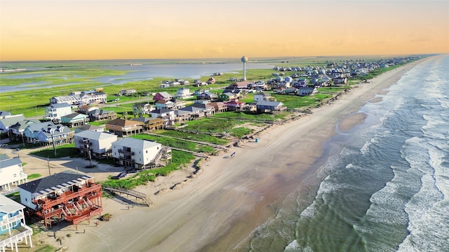 aerial view at dusk featuring a water view and a view of the beach