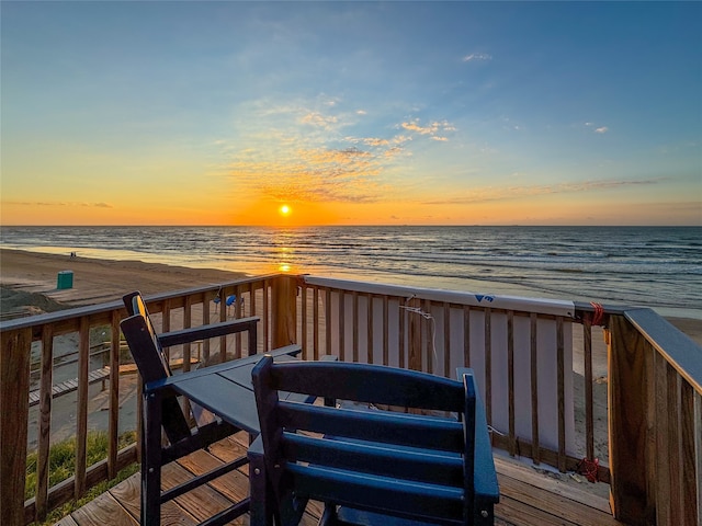 deck at dusk featuring a water view and a beach view