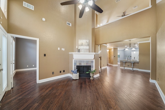 unfurnished living room with ceiling fan, a towering ceiling, dark wood-type flooring, and a tile fireplace