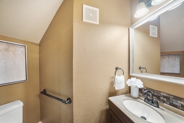 bathroom featuring vaulted ceiling, vanity, toilet, and tasteful backsplash