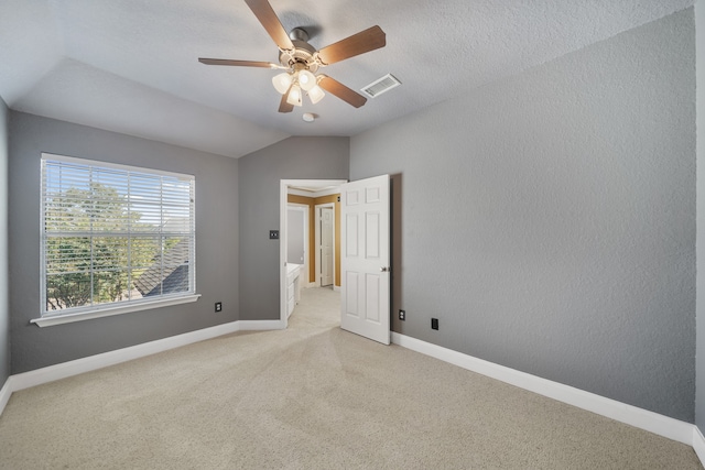 empty room featuring a textured ceiling, vaulted ceiling, ceiling fan, and light colored carpet