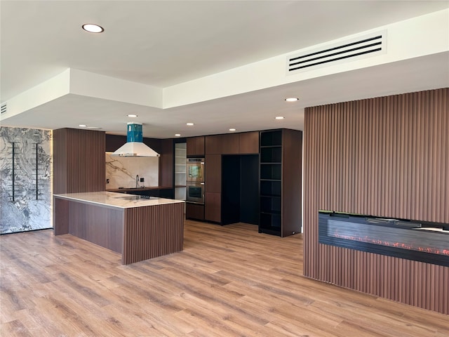 kitchen featuring tasteful backsplash, range hood, light hardwood / wood-style floors, dark brown cabinetry, and double oven