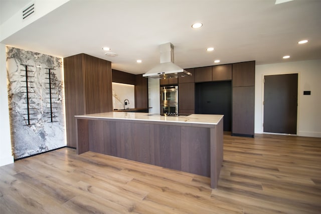 kitchen with ventilation hood, light hardwood / wood-style flooring, dark brown cabinetry, and stainless steel double oven