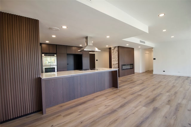 kitchen featuring light hardwood / wood-style floors, black electric cooktop, stainless steel double oven, and island range hood