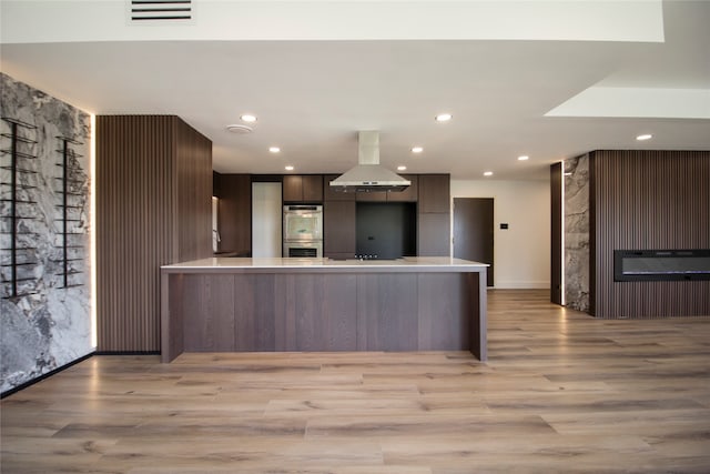 kitchen with light hardwood / wood-style floors, double oven, kitchen peninsula, and island range hood