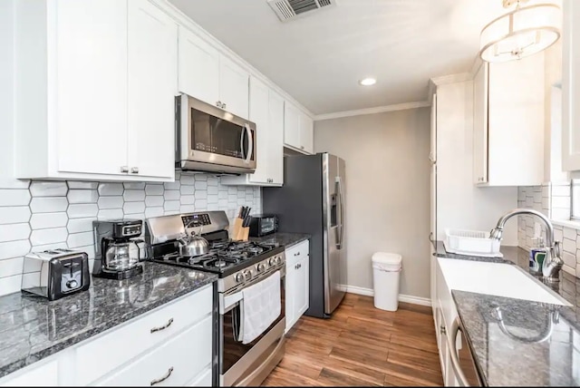 kitchen with decorative backsplash, hanging light fixtures, white cabinetry, light wood-type flooring, and stainless steel appliances