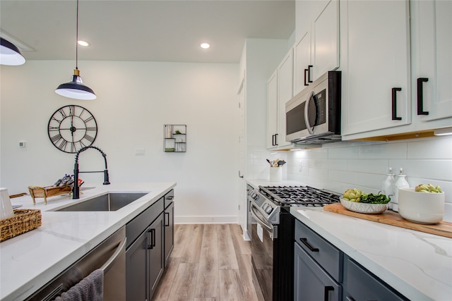 kitchen with sink, decorative light fixtures, appliances with stainless steel finishes, light stone countertops, and light hardwood / wood-style floors