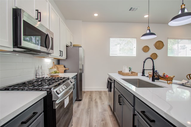 kitchen with sink, decorative light fixtures, white cabinetry, stainless steel appliances, and light wood-type flooring