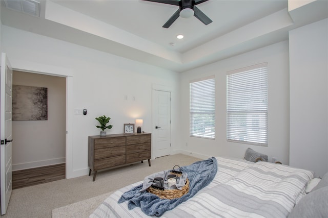 carpeted bedroom featuring a tray ceiling and ceiling fan