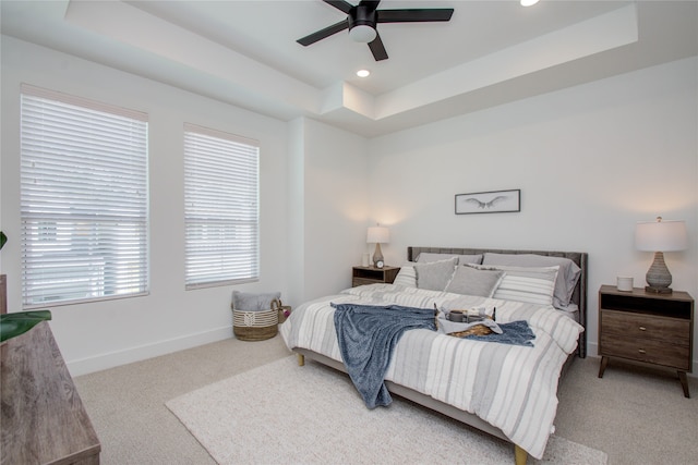 bedroom featuring light carpet, a tray ceiling, and ceiling fan