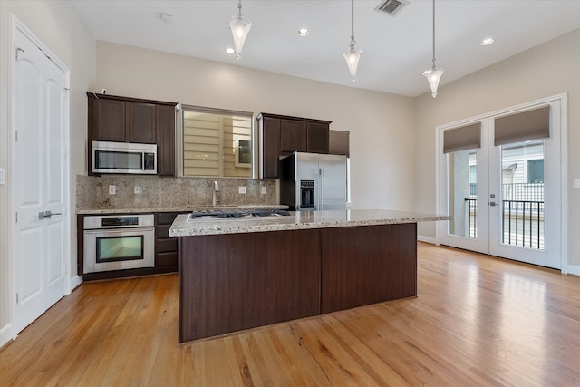 kitchen featuring dark brown cabinetry, tasteful backsplash, light hardwood / wood-style floors, decorative light fixtures, and appliances with stainless steel finishes