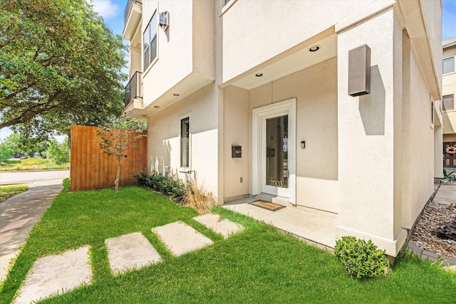 doorway to property featuring a lawn, fence, and stucco siding