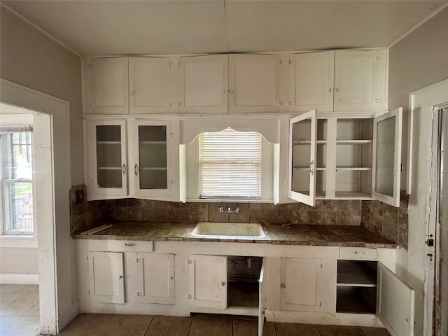 kitchen featuring decorative backsplash, white cabinets, light tile patterned floors, and sink