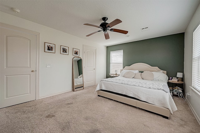 bedroom with ceiling fan, light colored carpet, and a textured ceiling