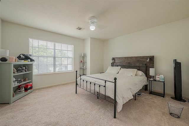 bedroom with ceiling fan, light colored carpet, and a textured ceiling