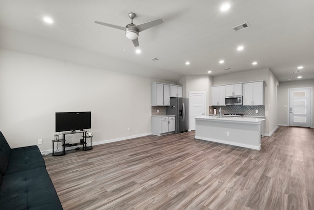 kitchen featuring light wood-type flooring, white cabinets, a center island with sink, appliances with stainless steel finishes, and ceiling fan