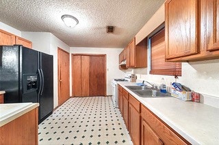 kitchen with a textured ceiling, stainless steel range oven, black fridge, and sink