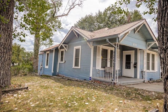 bungalow-style home with roof with shingles, a porch, and a front yard