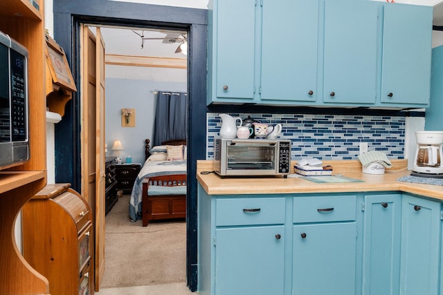 kitchen featuring blue cabinets, decorative backsplash, light countertops, and light carpet