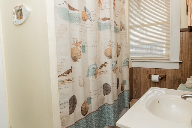 full bathroom with curtained shower, wood walls, and a sink