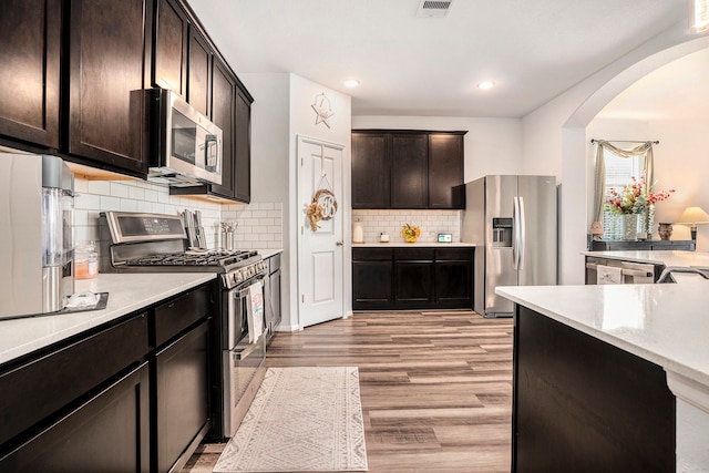 kitchen featuring dark brown cabinetry, stainless steel appliances, tasteful backsplash, and light hardwood / wood-style floors