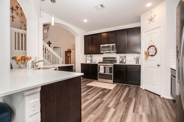 kitchen with dark brown cabinetry, sink, kitchen peninsula, decorative light fixtures, and appliances with stainless steel finishes