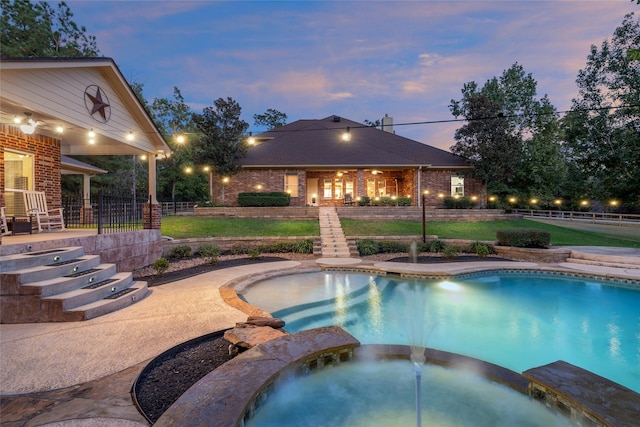 pool at dusk featuring an in ground hot tub, a patio area, and a yard