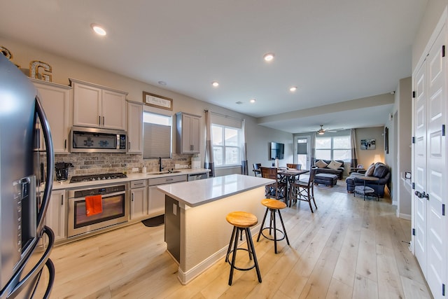 kitchen with tasteful backsplash, a breakfast bar, stainless steel appliances, light countertops, and light wood-type flooring