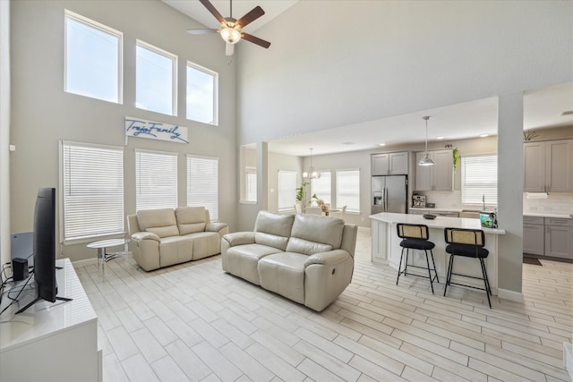 living room featuring ceiling fan with notable chandelier, a high ceiling, sink, and light wood-type flooring