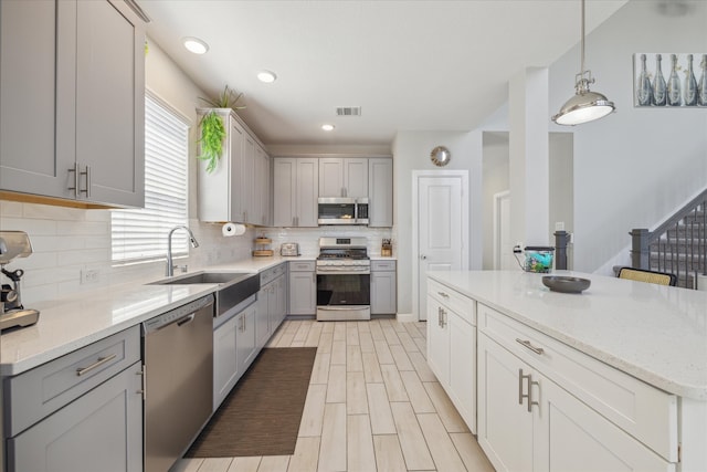 kitchen with pendant lighting, sink, gray cabinetry, backsplash, and stainless steel appliances