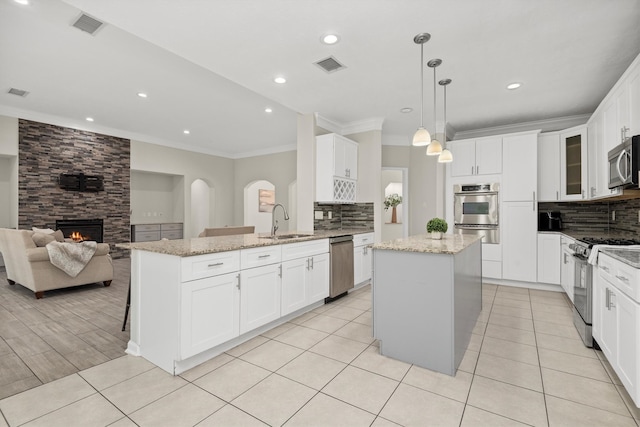 kitchen with light stone counters, a kitchen island, decorative light fixtures, stainless steel appliances, and a large fireplace