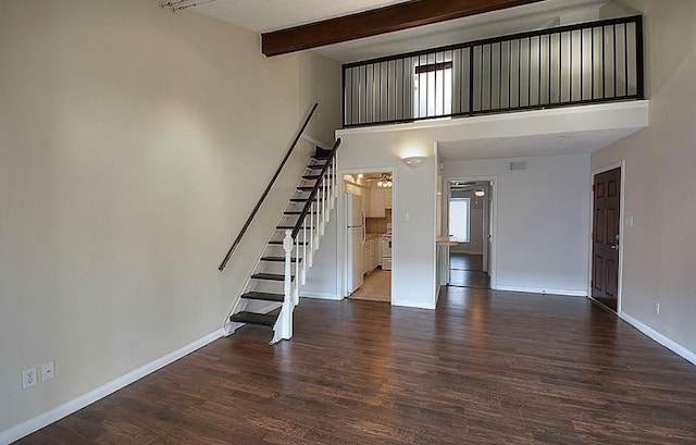 unfurnished living room featuring a towering ceiling, beam ceiling, and dark hardwood / wood-style flooring