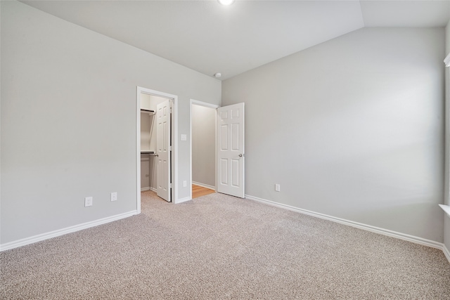 unfurnished bedroom with light carpet, a closet, vaulted ceiling, and a spacious closet