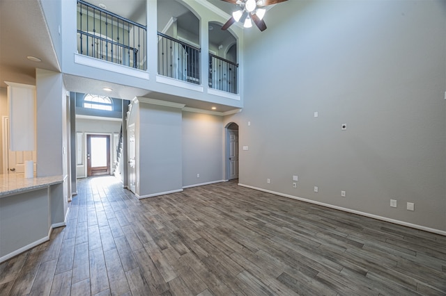 unfurnished living room featuring a high ceiling, ceiling fan, and dark wood-type flooring