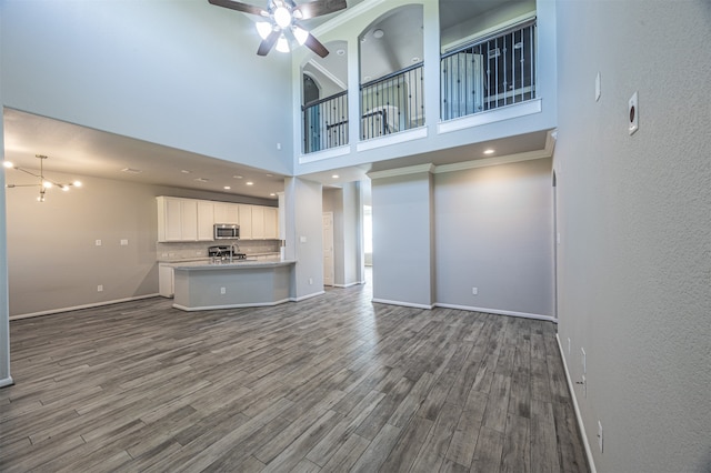 unfurnished living room featuring ceiling fan with notable chandelier, a high ceiling, wood-type flooring, and ornamental molding