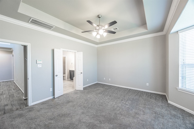 unfurnished bedroom featuring crown molding, a tray ceiling, dark colored carpet, and ceiling fan