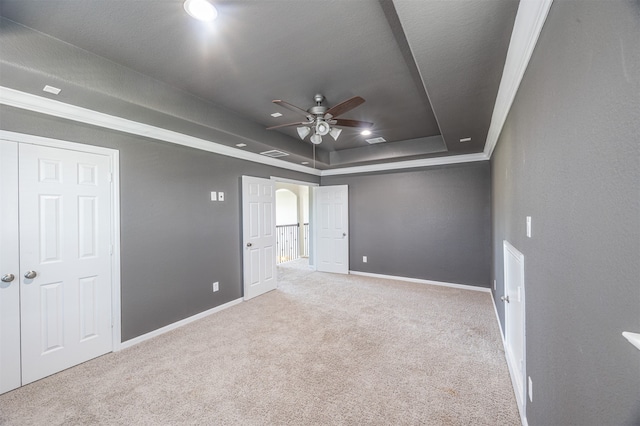 spare room with light carpet, a tray ceiling, ceiling fan, and ornamental molding