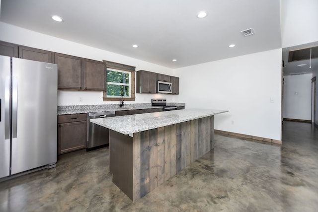 kitchen with light stone counters, a center island, sink, appliances with stainless steel finishes, and dark brown cabinetry