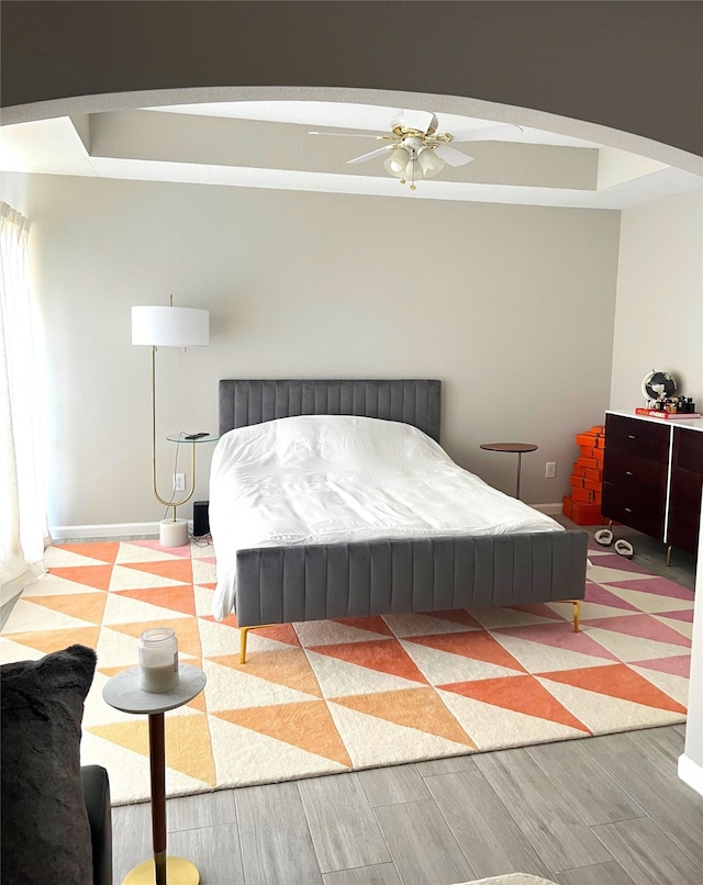 bedroom featuring a raised ceiling, ceiling fan, and light hardwood / wood-style flooring