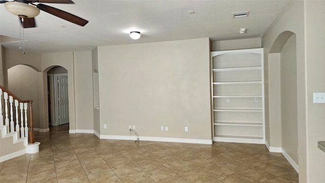 tiled empty room with ceiling fan and built in shelves