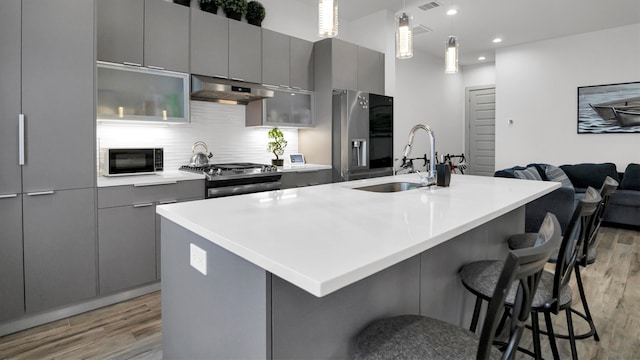 kitchen with gray cabinets, a breakfast bar, sink, a center island with sink, and appliances with stainless steel finishes