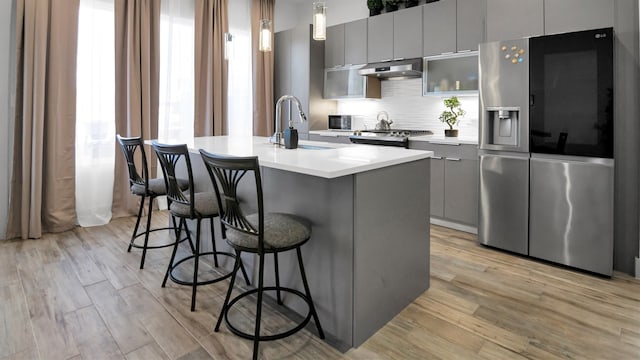 kitchen with appliances with stainless steel finishes, a kitchen island with sink, gray cabinets, and a wealth of natural light