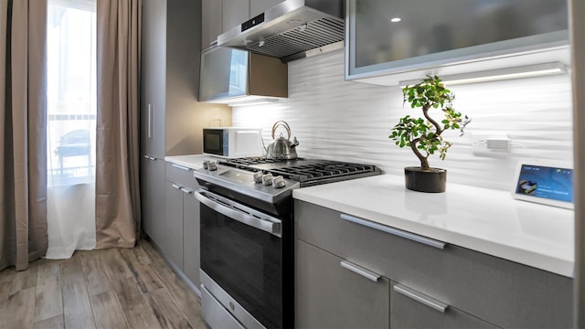 kitchen featuring light hardwood / wood-style floors, stainless steel range with gas cooktop, ventilation hood, gray cabinetry, and backsplash