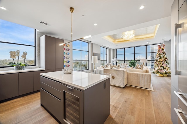 kitchen with light wood-type flooring, a tray ceiling, hanging light fixtures, a center island, and plenty of natural light