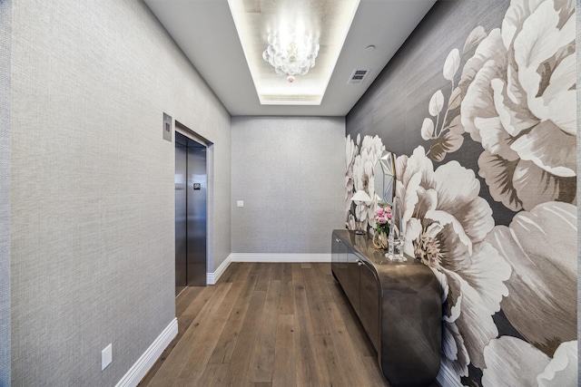 hall with a chandelier, hardwood / wood-style flooring, a raised ceiling, and elevator