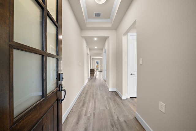 hallway featuring a raised ceiling, ornamental molding, and light wood-type flooring