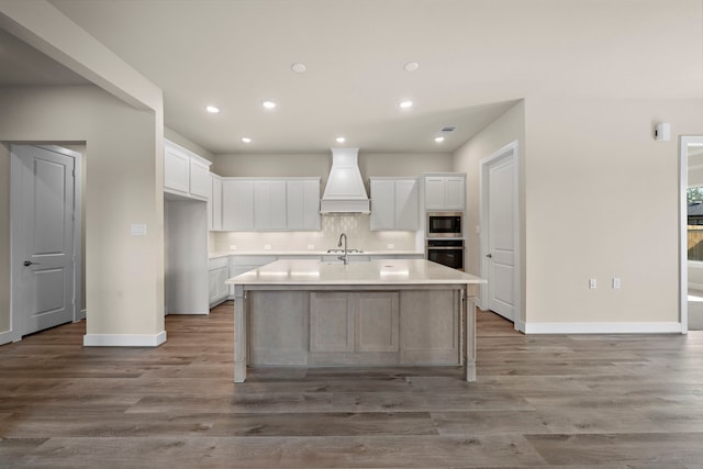 kitchen with a center island with sink, white cabinetry, stainless steel appliances, and custom range hood