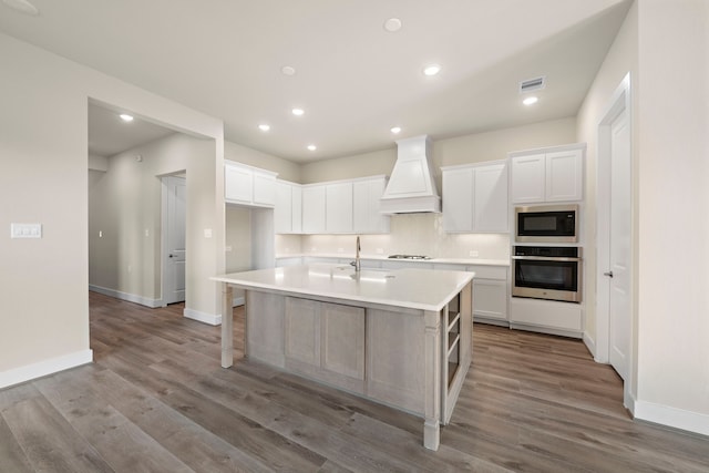 kitchen with stainless steel appliances, a center island with sink, custom range hood, and white cabinetry