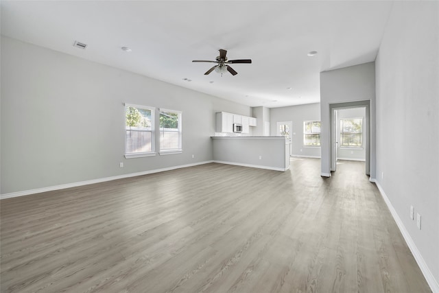 unfurnished living room with light wood-type flooring, plenty of natural light, baseboards, and ceiling fan