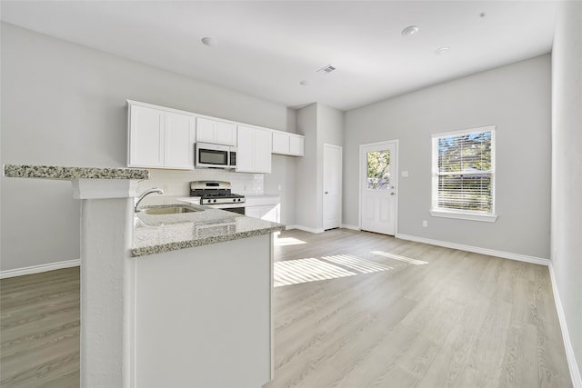 kitchen with light stone counters, white cabinets, stainless steel appliances, light hardwood / wood-style flooring, and sink